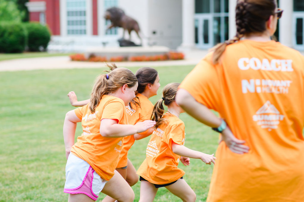 Two Girls on the Run participants smile at the camera while running at an outdoor practice in yellow shirts